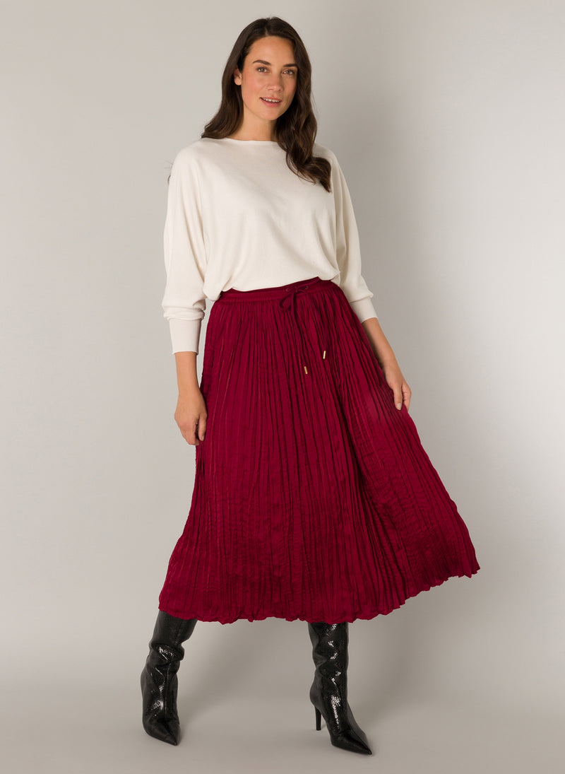 Red pleated skirt from Yest shown on a model with a cream batwing top